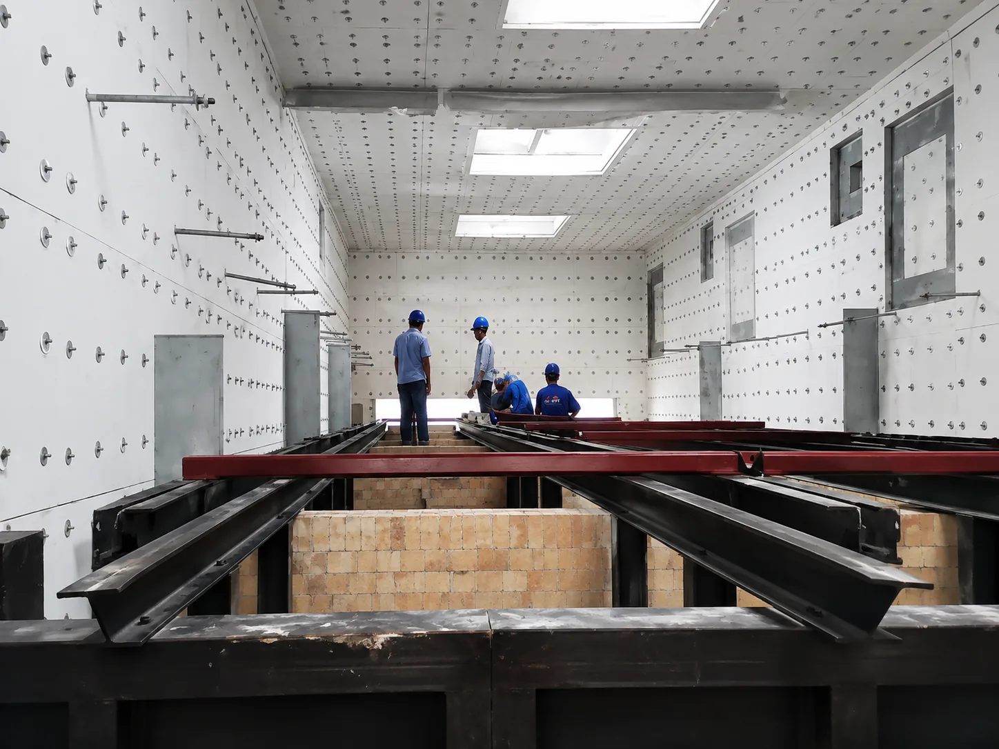 Technicians inside a large refractory-lined heat treatment furnace chamber during construction