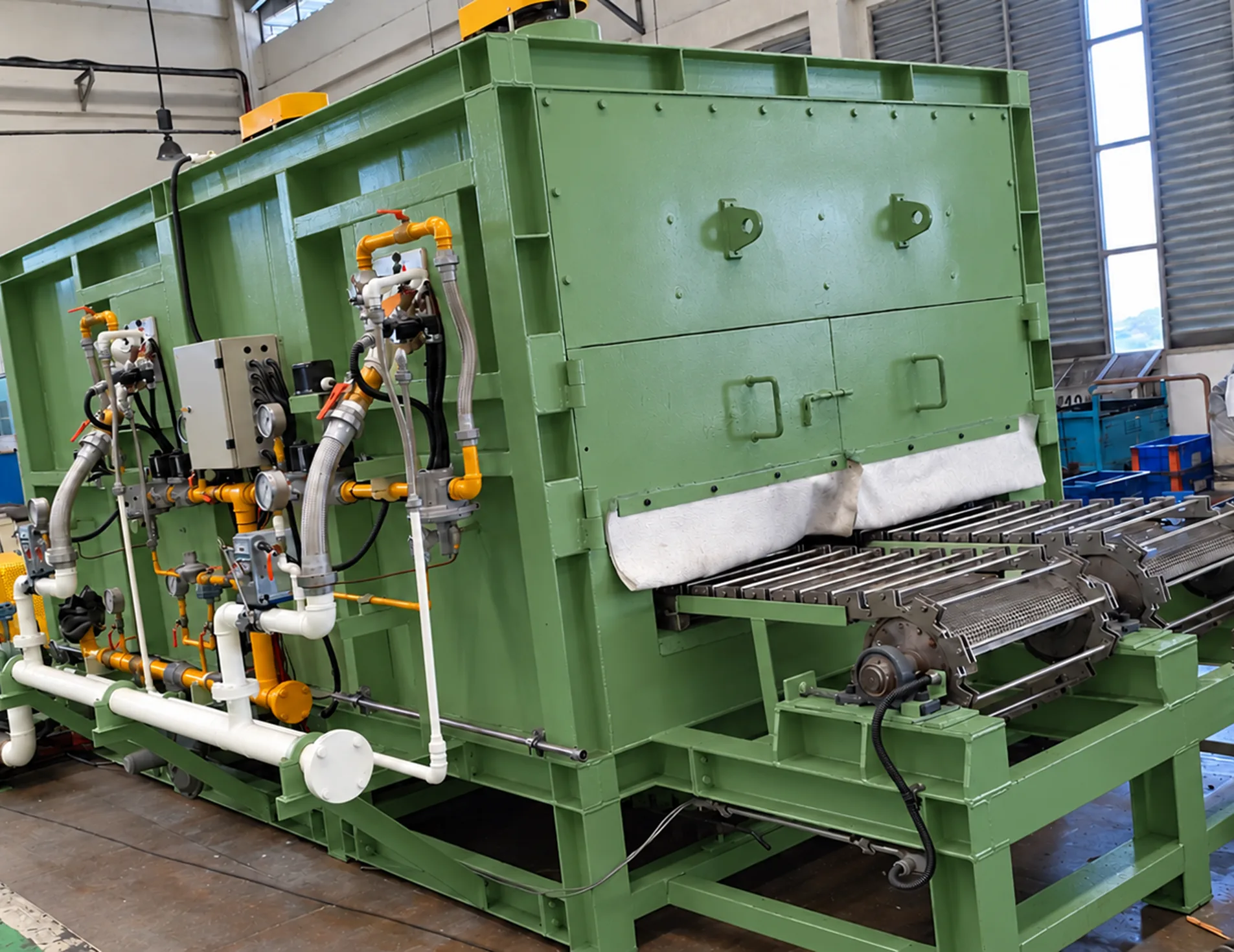 MWT green industrial furnace with gas train piping, control box and conveyor belt on the plant floor
